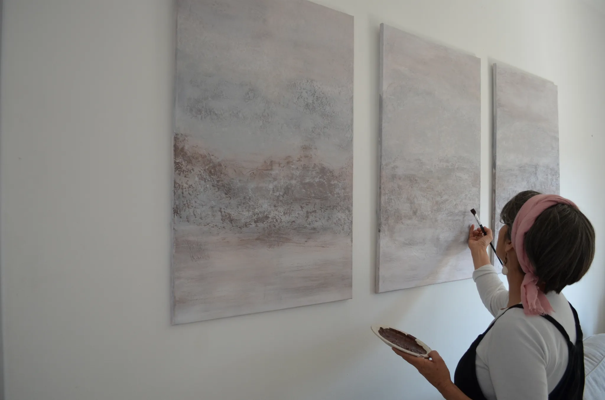Sonja at work in her sunlit studio, surrounded by textured paintings and art supplies