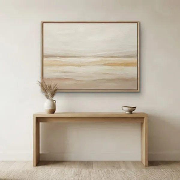 A finished landscape painting hanging above a simple wooden console table