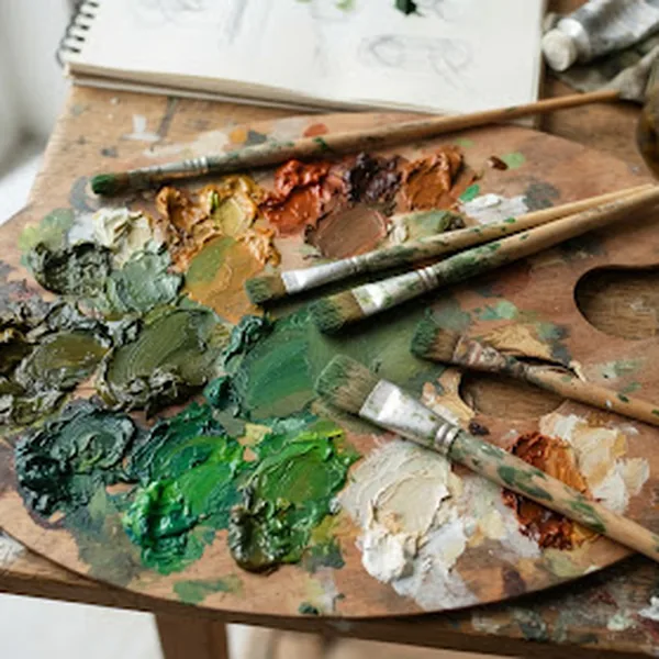An artist's palette of mixed paints in deep olive and warm neutrals with fine art brushes