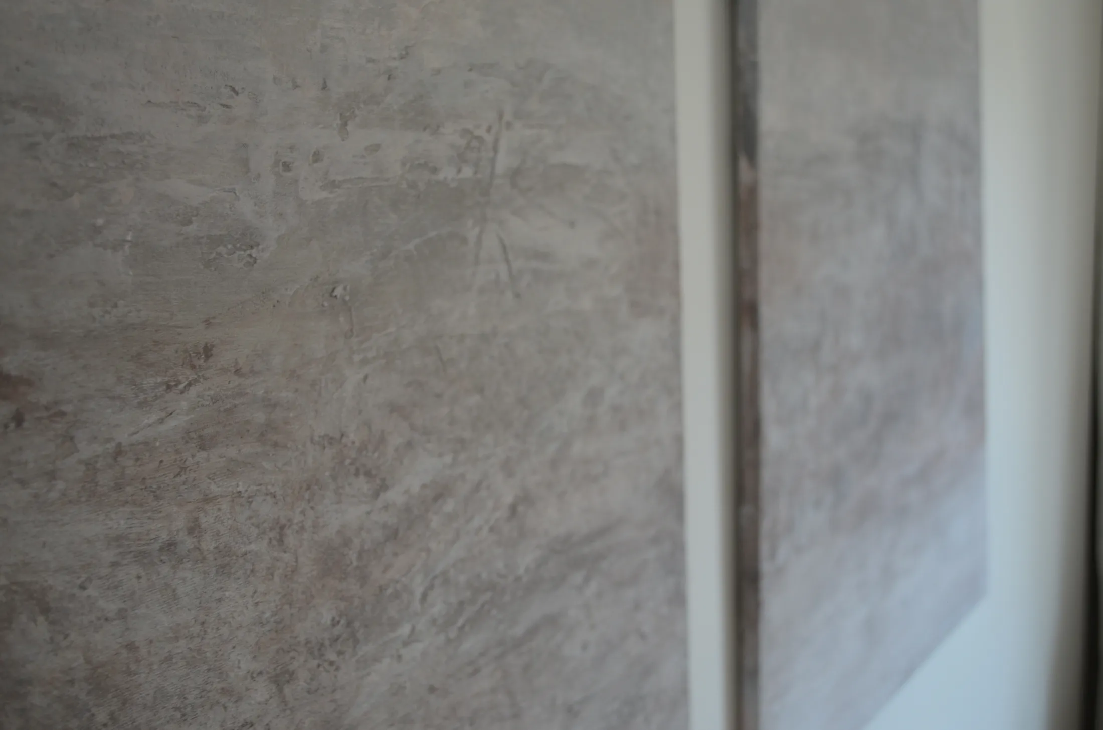 Close-up of Misty Horizon's heavily textured plaster surface in soft grey and blush tones, with the neighbouring panel visible in soft focus